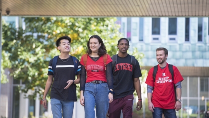 three male and one female student walking on campus wearing Rutgers t-shirts