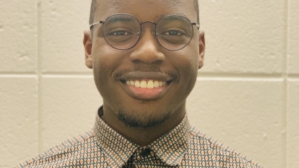 Head shot of Black young man wearing glasses and a light brown collared shirt.