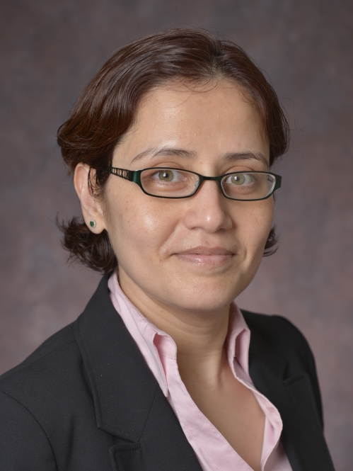headshot of woman with short brown hair and glasses wearing a dark suit jacket and pink shirtt