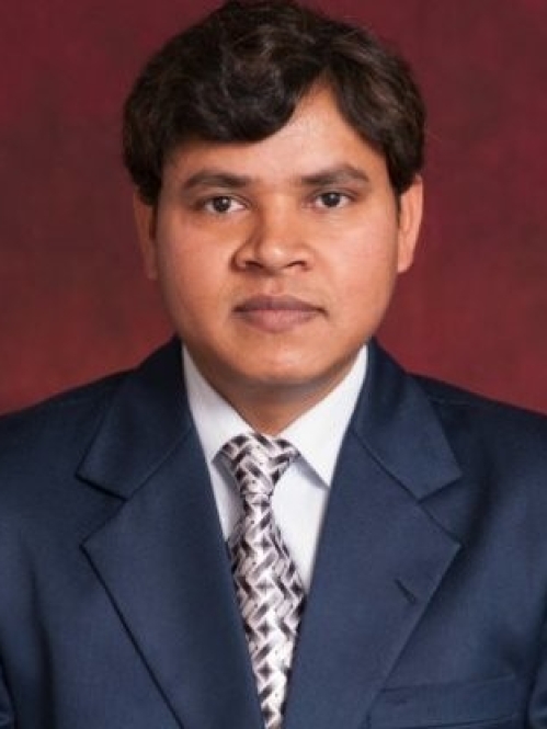 Head shot of Indian man with short dark brown hair, wearing a blue suit, white shirt, and patterned tie.