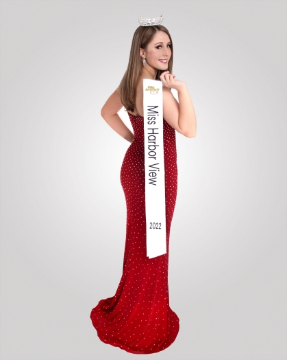 Female in long red gown with a crown on her head holding a white Miss Harbor View sash over her sholder.
