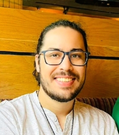 Young white male with black beard and hair, wearing glasses and gray shirt.